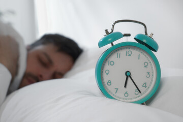 Canvas Print - Sleepy man awaking at home in morning, focus on alarm clock. Space for text