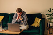 © Diana Vyshniakova - Sad, frustrated man sitting on the green couch in his living room in front of his laptop.