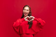 Young asian woman wearing red sweater dress shapes heart gesture on red background for Chinese new year and Christmas festival