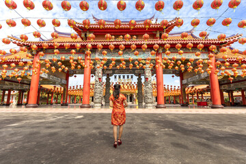 Rear view of Asian woman in red cheongsam qipao dress is visiting the Chinese Buddhist temple during lunar new year for traditional culture concept