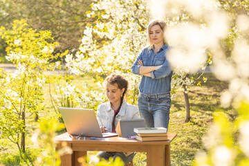 Wall Mural - Woman and little girl laying on the spring flower field outdoors - having fun using a laptop.