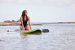 Woman surfing, sea and exercise with surfboard or paddleboard, swimwear and focus with sport outdoor and nature. Beach, fitness and young female surfer, waves and adventure with extreme sports