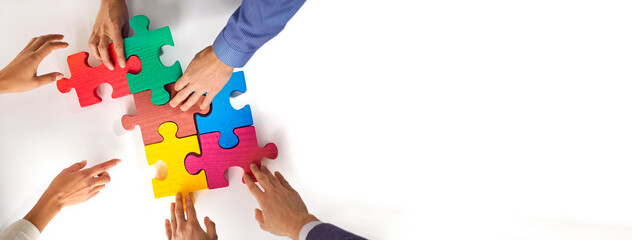 Business team matching jigsaw puzzle parts. Young people connect colorful red, green, pink, blue, yellow jigsaw pieces on white office table. Crop shot. Teamwork concept. Copy space banner background