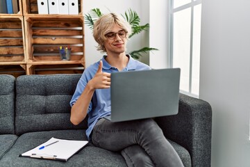 Sticker - Young man working using computer laptop sitting on the sofa smiling happy and positive, thumb up doing excellent and approval sign