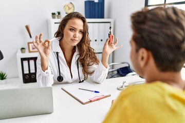 Canvas Print - Young doctor woman showing electronic cigarette and normal cigarrete to patient relaxed with serious expression on face. simple and natural looking at the camera.