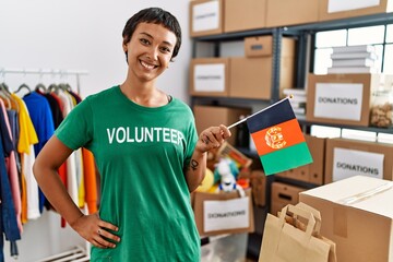 Sticker - Young hispanic woman wearing volunteer uniform holding afghanistan flag at charity center