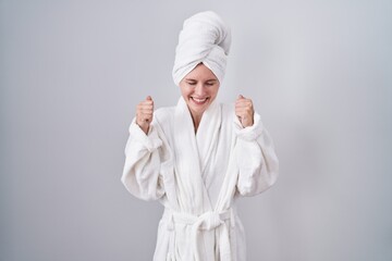 Poster - Blonde caucasian woman wearing bathrobe excited for success with arms raised and eyes closed celebrating victory smiling. winner concept.