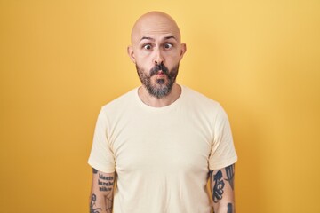 Poster - Hispanic man with tattoos standing over yellow background making fish face with lips, crazy and comical gesture. funny expression.