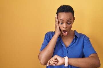 Wall Mural - African american woman standing over yellow background looking at the watch time worried, afraid of getting late