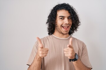 Wall Mural - Hispanic man with curly hair standing over white background pointing fingers to camera with happy and funny face. good energy and vibes.