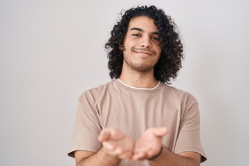 Hispanic man with curly hair standing over white background smiling with hands palms together receiving or giving gesture. hold and protection