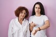 © Krakenimages.com - Hispanic mother and daughter wearing casual white t shirt over pink background in hurry pointing to watch time, impatience, upset and angry for deadline delay