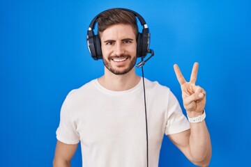 Poster - Hispanic man with beard listening to music wearing headphones showing and pointing up with fingers number two while smiling confident and happy.