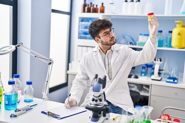 Canvas Print - Young hispanic man scientist writing on document holding urine test tube at laboratory