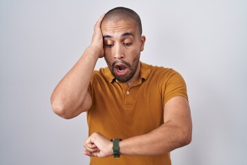 Sticker - Hispanic man with beard standing over white background looking at the watch time worried, afraid of getting late