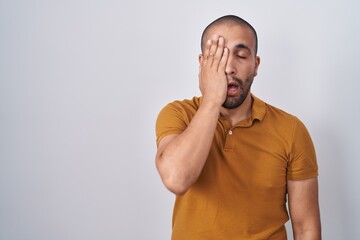 Sticker - Hispanic man with beard standing over white background yawning tired covering half face, eye and mouth with hand. face hurts in pain.