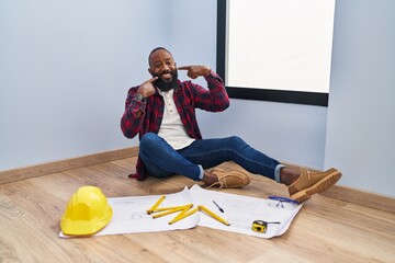 Sticker - African american man sitting on the floor at new home looking at blueprints smiling cheerful showing and pointing with fingers teeth and mouth. dental health concept.