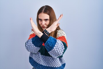 Poster - Young hispanic girl standing over blue background rejection expression crossing arms doing negative sign, angry face