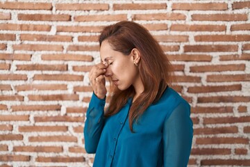 Sticker - Brunette woman standing over bricks wall tired rubbing nose and eyes feeling fatigue and headache. stress and frustration concept.