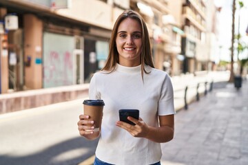 Wall Mural - Young blonde woman using smartphone and drinking coffee at street