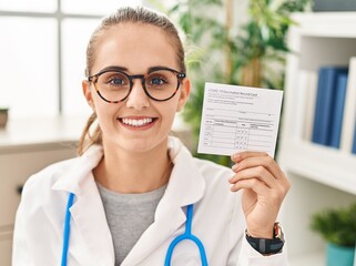 Canvas Print - Young doctor woman holding covid certificate looking positive and happy standing and smiling with a confident smile showing teeth