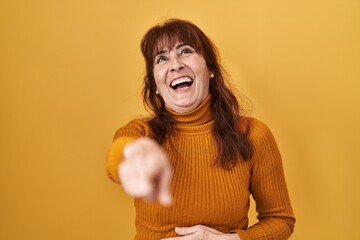 Canvas Print - Middle age hispanic woman standing over yellow background laughing at you, pointing finger to the camera with hand over body, shame expression