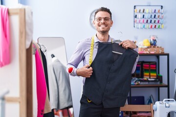 Young hispanic man tailor smiling confident holding waistcoat at tailor shop