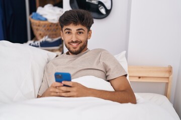 Sticker - Young arab man using smartphone sitting on bed at bedroom