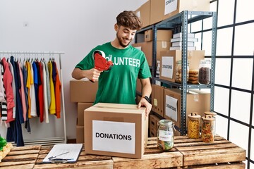 Sticker - Young arab man wearing volunteer uniform packing donations box at charity center