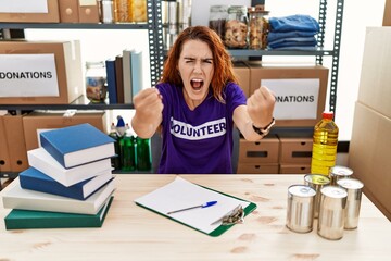 Sticker - Young redhead woman wearing volunteer t shirt at donations stand angry and mad raising fists frustrated and furious while shouting with anger. rage and aggressive concept.