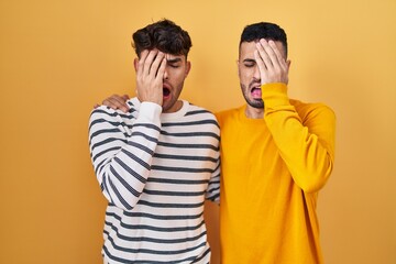 Wall Mural - Young hispanic gay couple standing over yellow background yawning tired covering half face, eye and mouth with hand. face hurts in pain.