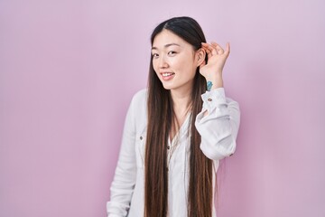 Sticker - Chinese young woman standing over pink background smiling with hand over ear listening an hearing to rumor or gossip. deafness concept.