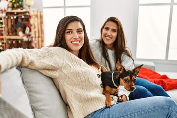 Poster - Two women smiling confident sitting with dog by christmas decor at home