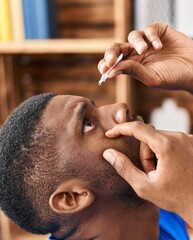 Wall Mural - Young african american man applying eye drop sitting on sofa at home