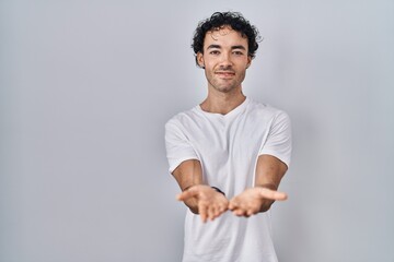 Wall Mural - Hispanic man standing over isolated background smiling with hands palms together receiving or giving gesture. hold and protection