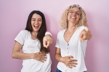 Sticker - Mother and daughter standing together over pink background laughing at you, pointing finger to the camera with hand over body, shame expression