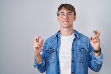 Sticker - Caucasian blond man standing wearing glasses gesturing finger crossed smiling with hope and eyes closed. luck and superstitious concept.