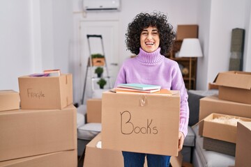 Sticker - Young brunette woman with curly hair moving to a new home holding cardboard box smiling and laughing hard out loud because funny crazy joke.