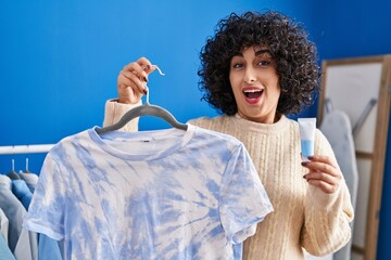 Poster - Young brunette woman with curly hair dyeing tye die t shirt celebrating crazy and amazed for success with open eyes screaming excited.