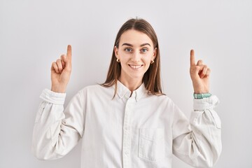 Poster - Young caucasian woman standing over isolated background smiling amazed and surprised and pointing up with fingers and raised arms.