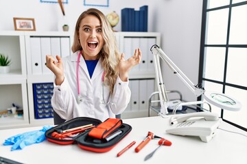 Sticker - Young beautiful doctor woman with reflex hammer and medical instruments celebrating surprised and amazed for success with arms raised and open eyes. winner concept.