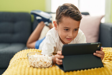 Sticker - Adorable hispanic toddler watching video on touchpad lying on sofa at home