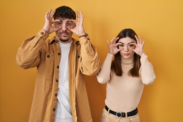 Poster - Young hispanic couple standing over yellow background trying to open eyes with fingers, sleepy and tired for morning fatigue