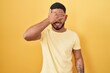 © Krakenimages.com - Young hispanic man standing over yellow background smiling and laughing with hand on face covering eyes for surprise. blind concept.