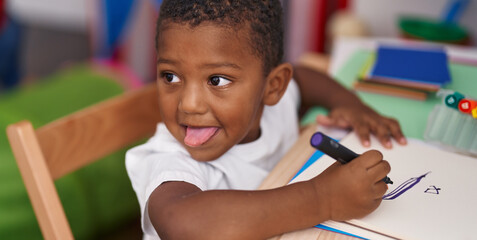 Sticker - African american boy preschool student sitting on table drawing on notebook at kindergarten