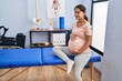 © Krakenimages.com - Young latin woman pregnant patient sitting on massage table at clinic