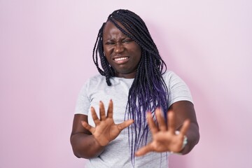 Wall Mural - Young african woman standing over pink background disgusted expression, displeased and fearful doing disgust face because aversion reaction.