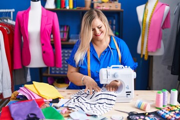 Young woman tailor smiling confident using sewing machine at sewing studio