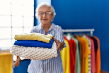 Wall Mural - Senior grey-haired woman smiling confident holding folded clothes at laundry room