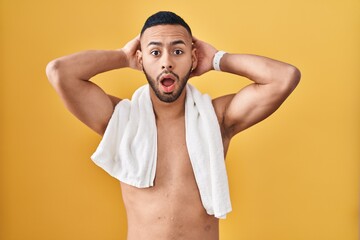 Canvas Print - Young hispanic man standing shirtless with towel crazy and scared with hands on head, afraid and surprised of shock with open mouth